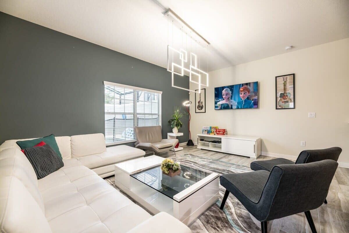 Un saló modern amb un sofà blanc, una taula de centre de vidre i un butac armchair gris. Hi ha quadres emmarcats a la paret i una planta sobre una taula auxiliar.