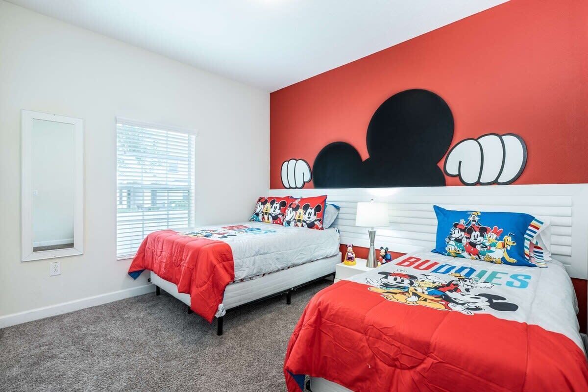 Une chambre avec deux lits, chacun agrémenté de linge de lit aux motifs de Mickey Mouse.