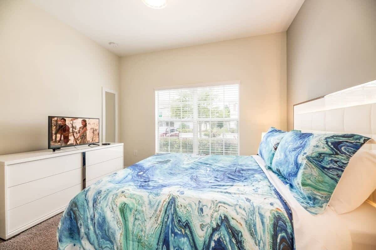 Een slaapkamer met een bed, een dressoir, een televisie en een raam.