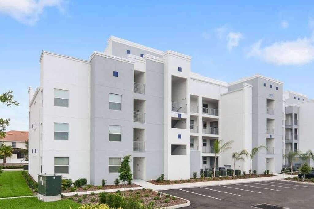 A multi-story building with a modern design, featuring balconies and a parking lot in front.