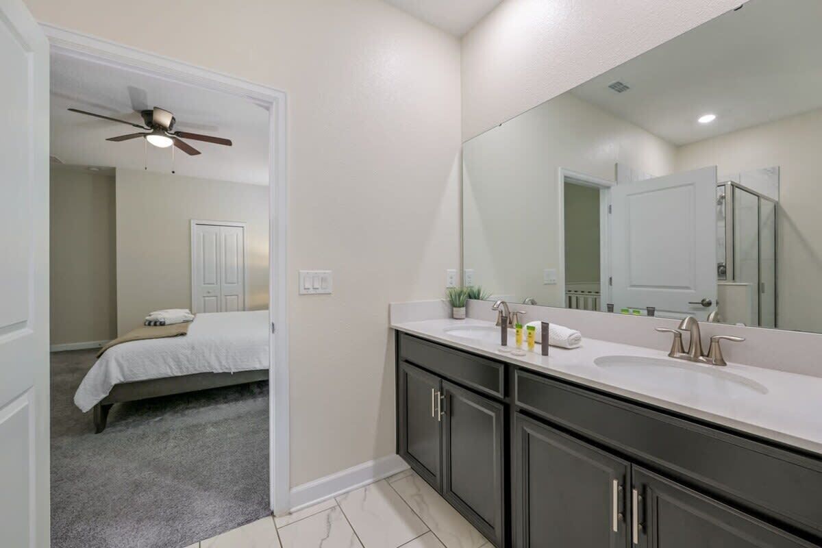 A modern bathroom with a large mirror, dark cabinets, and a white countertop.