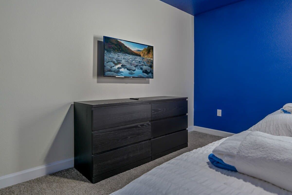 A bedroom with a bed, a dresser, a TV mounted on the wall, and a blue accent wall.