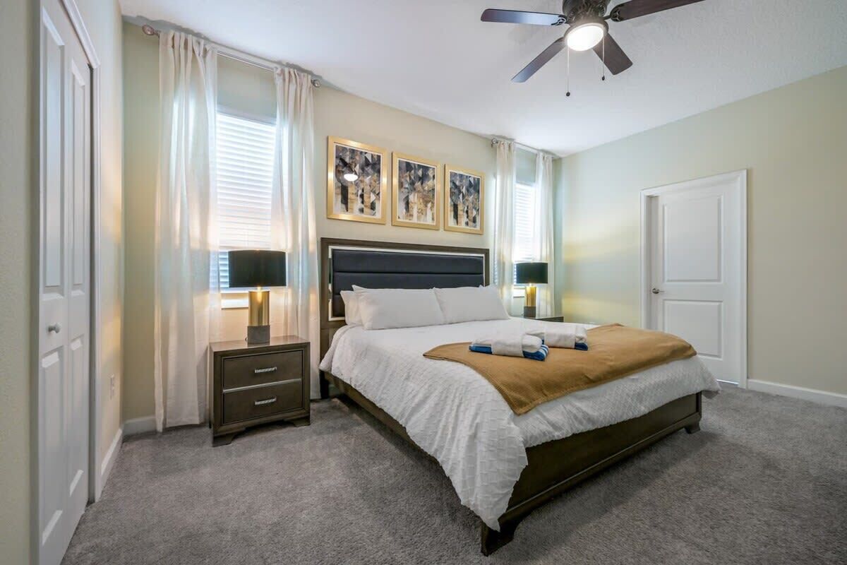 A bedroom with a bed, bedside tables, a ceiling fan, and artwork on the wall.