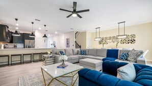A modern living room with a sectional sofa, a coffee table, and a kitchen area with bar stools. - Disney Bliss Themed Rooms, Game Room, Private Pool (Kissimmee)
