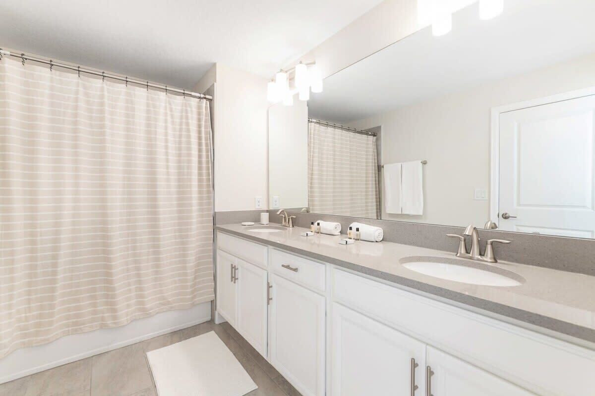 A modern bathroom with a double sink vanity, a large mirror, and a shower curtain.