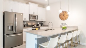 Una cocina moderna con electrodomésticos de acero inoxidable, una isla central con taburetes de bar y un reloj de pared.