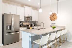 A modern kitchen with stainless steel appliances, a central island with bar stools, and a wall clock. - Disney Dream Home, Prime Location, Private Pool (Kissimmee)