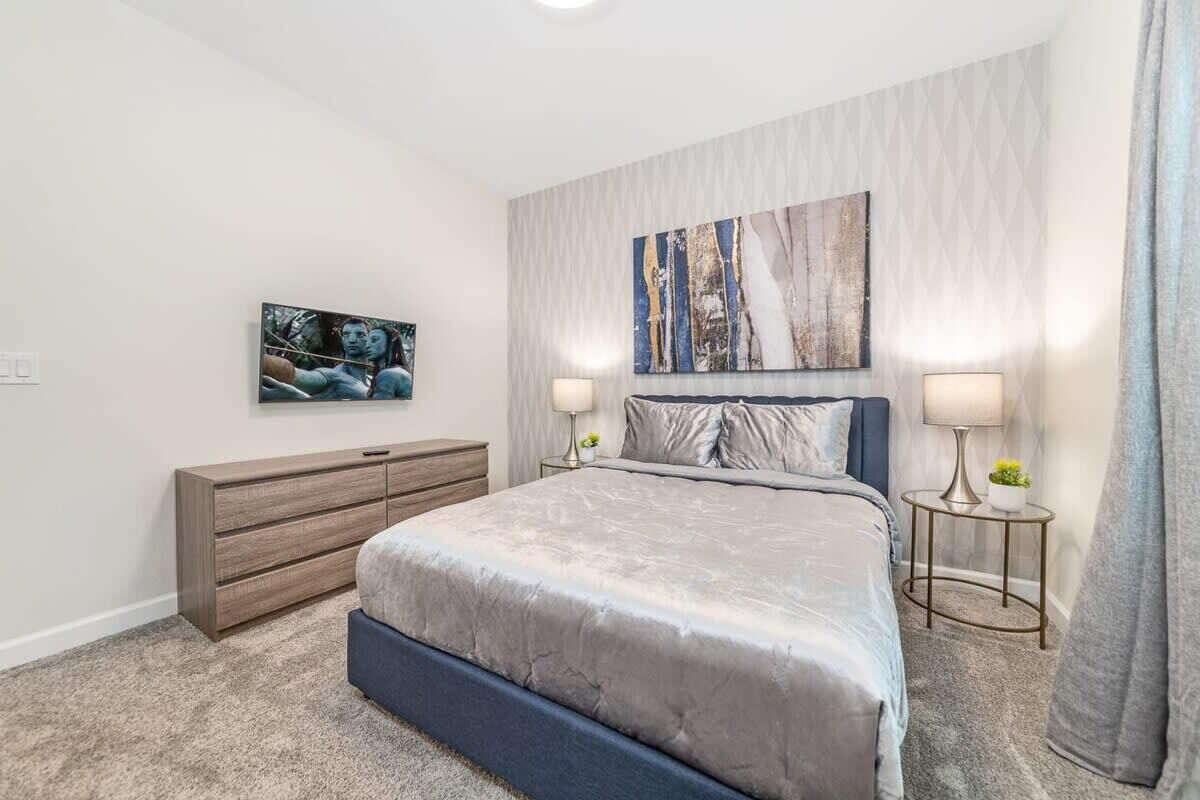 Een slaapkamer met een groot bed, een dressoir, twee nachtkastjes met lampen en een aan de muur bevestigde televisie.