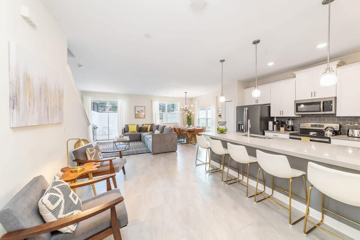 Una cocina moderna con una isla central, taburetes de bar y una zona de comedor con mesa y sillas.