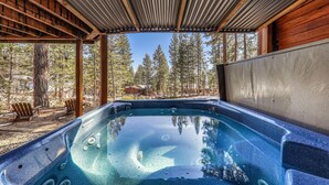 Un bain à remous avec une terrasse en bois et des chaises, entouré d’arbres et sous un ciel dégagé.