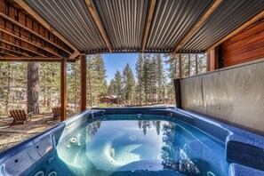 Ein Whirlpool mit Holzterrasse und Stühlen, umgeben von Bäumen und einem klaren Himmel.