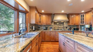 Une cuisine dotée de meubles en bois, de plans de travail en granit, d’une cuisinière encastrée et d’une grande fenêtre.