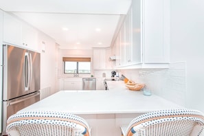A modern kitchen with white cabinetry, stainless steel appliances, and a large island with seating. - Shipwatch D603 (Pensacola)