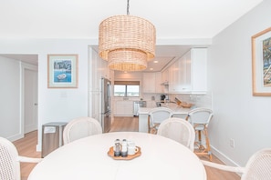 A modern kitchen with white cabinets, a stainless steel refrigerator, and a hanging woven light fixture. - Shipwatch D603 (Pensacola)