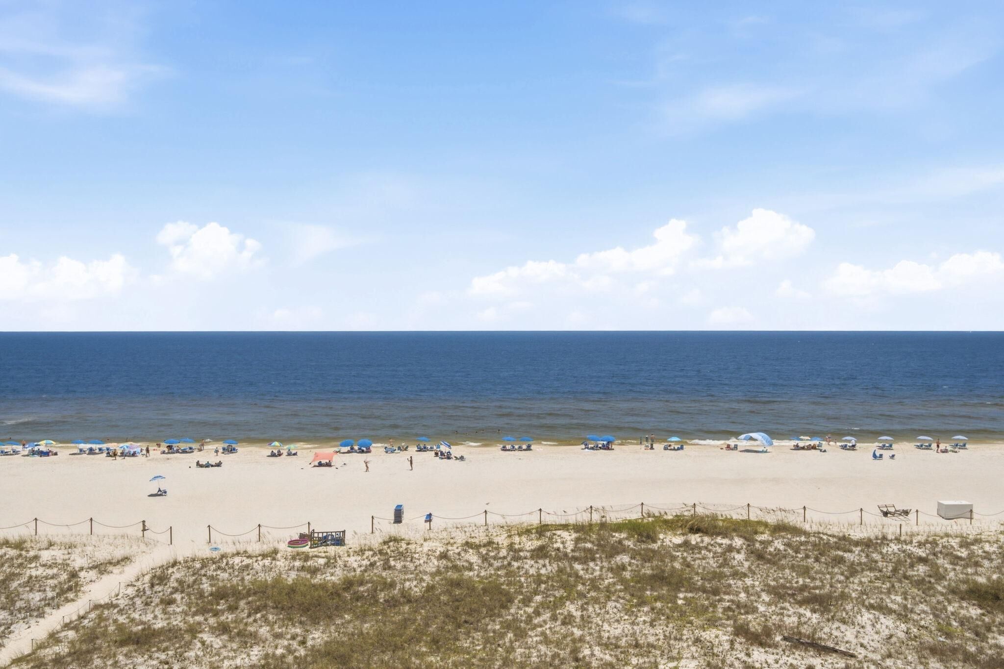 A beach with a fence, beach umbrellas, and a clear sky.