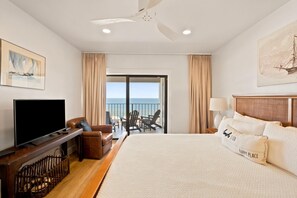 Une chambre d’hôtel avec un lit, une télévision, un bureau, une chaise, un balcon donnant sur la mer et un tableau au mur.