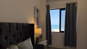A bedroom with a bed, a nightstand, a lamp, a painting, and a window with curtains. - Oceanview Condo in Palos Prietos | Pool + 1 Block to Beach (Mazatlán)