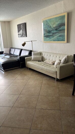 Ein Wohnzimmer mit einem beigen Sofa, einem schwarzen Ledersessel und einer Stehlampe.