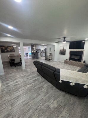 Ein geräumiger Wohnbereich mit einem dunklen Sofa, einem Esstisch und einer Küche im Hintergrund.