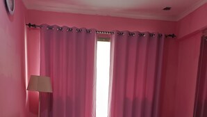 Un dormitorio con paredes rosadas, una cama, un televisor, una lámpara y una alfombra rosa.
