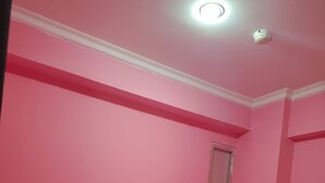 Una habitación rosa con una cama individual, una ventana pequeña y una lámpara en el techo.