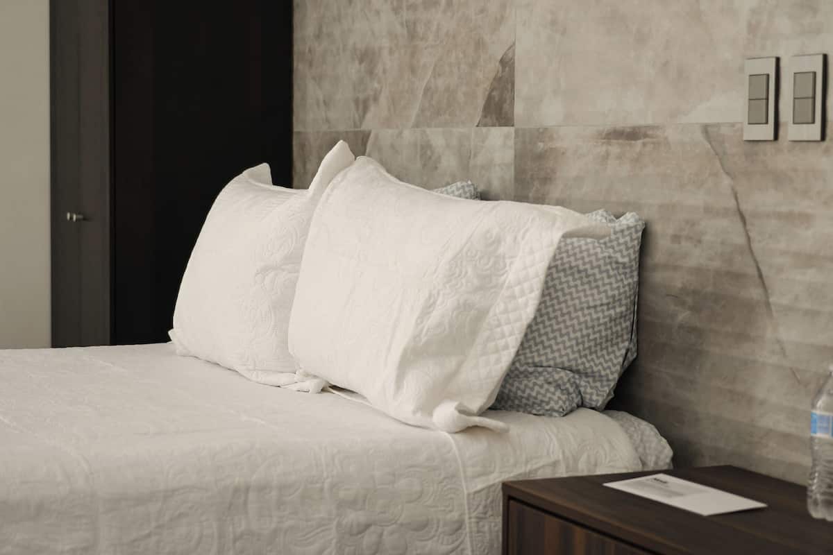 Une chambre d’hôtel avec un lit, une table de chevet, une armoire sombre et un mur en marbre.