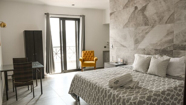 A hotel room with a bed, a desk, a chair, a sofa, a large window, and a view of the outdoors. - Hotel Asís (San Juan de los Lagos)