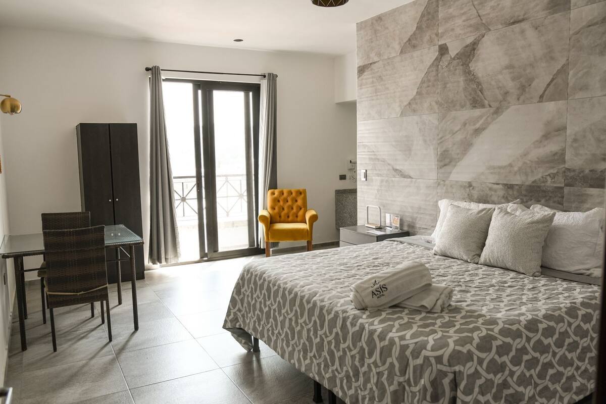 Une chambre d’hôtel équipée d’un lit, d’un bureau, d’une chaise, d’un canapé, d’une grande fenêtre et offrant une vue sur l’extérieur.