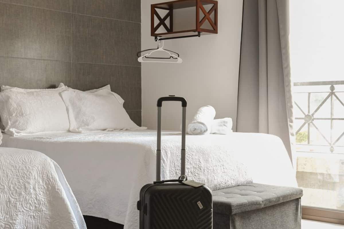 Une chambre d’hôtel avec un lit, une valise, une lampe suspendue et une vue sur l’extérieur.