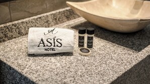 A hotel towel with 'ASÍS HOTEL' on it, two bottles of shampoo, and a large bowl on a granite countertop. - Hotel Asís (San Juan de los Lagos)