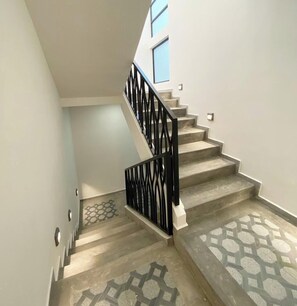 Una escalera con piso de diseño geométrico, barandal negro y una ventana en la parte superior.