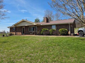 A single-story brick house with a front porch, a chimney, and a vehicle parked in the driveway. - Large brick home centrally located in Limestone. (Limestone)