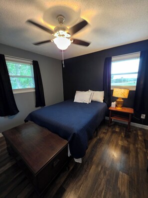 A bedroom with a bed, a nightstand, a desk, a ceiling fan, and two windows with curtains. - Large brick home centrally located in Limestone. (Limestone)