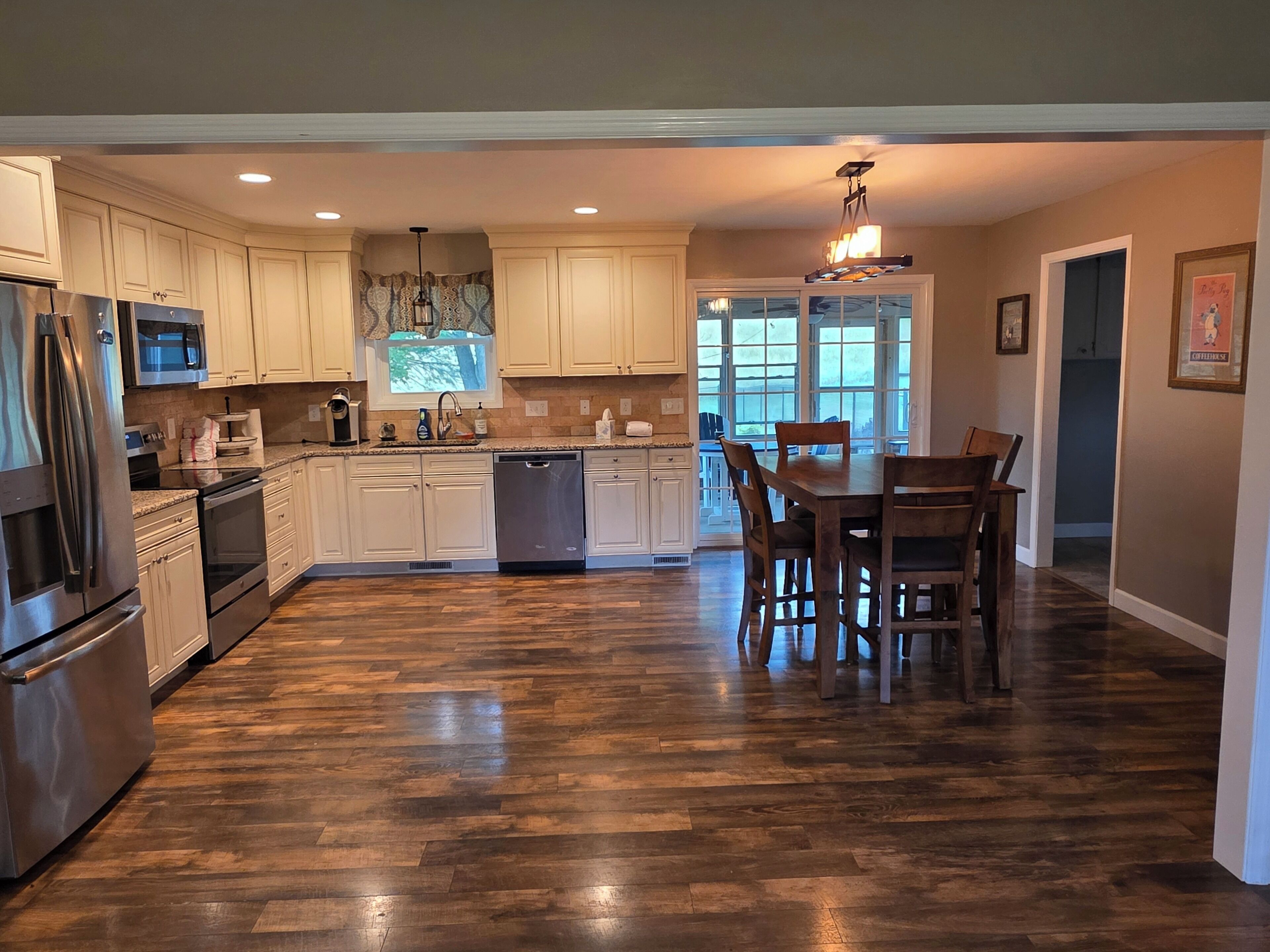 A modern kitchen with wooden flooring, white cabinetry, stainless steel appliances, and a dining area with a table and chairs.. Large brick home centrally located in Limestone.