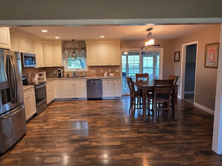 A modern kitchen with wooden flooring, white cabinetry, stainless steel appliances, and a dining area with a table and chairs.. Large brick home centrally located in Limestone.