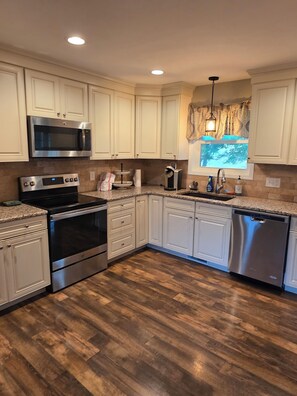 A kitchen with white cabinets, stainless steel appliances, a wooden floor, and a window with a view. - Large brick home centrally located in Limestone. (Limestone)