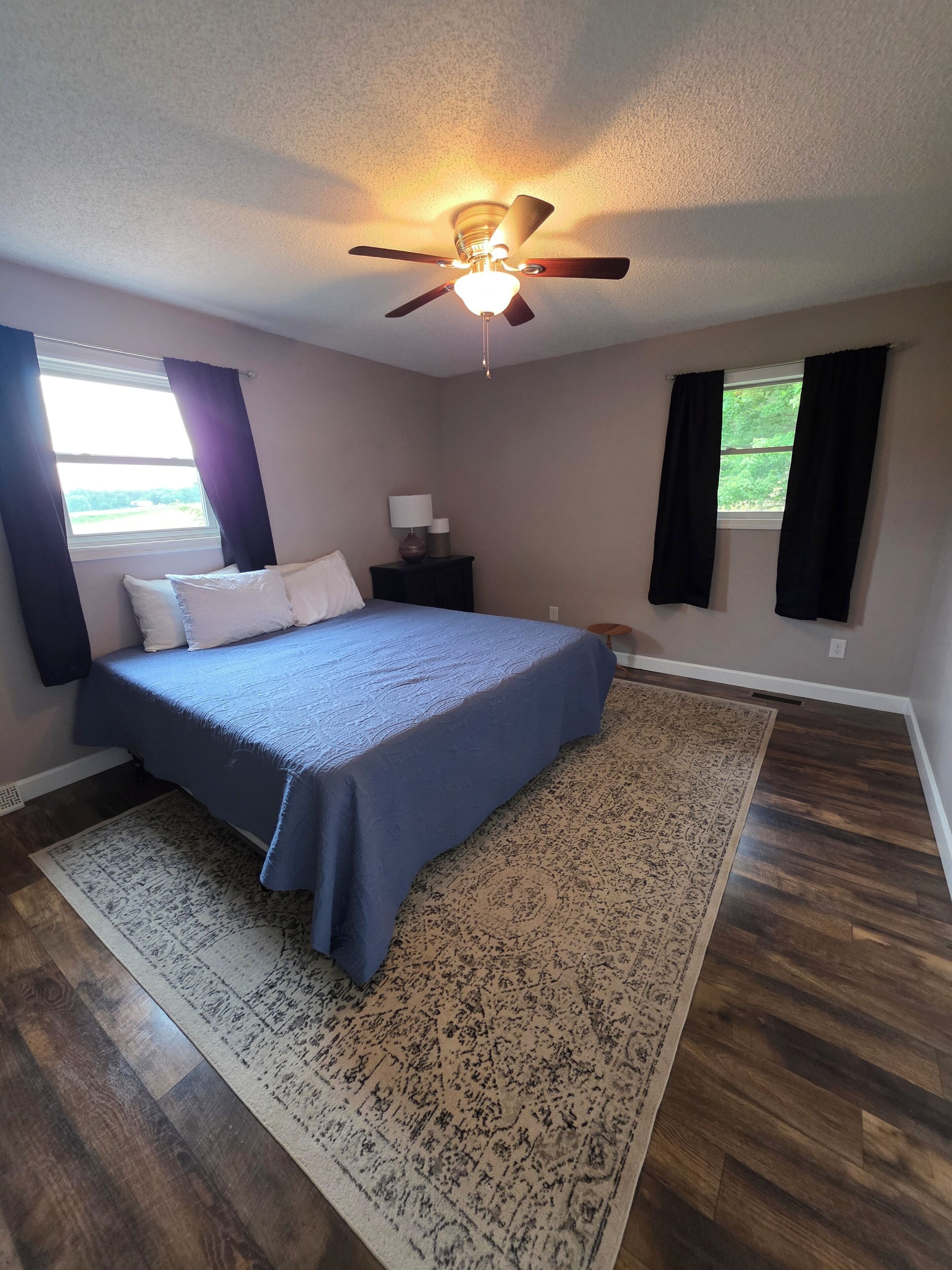 A bedroom with a bed, a ceiling fan, a nightstand, a window with curtains, and a patterned rug.. Large brick home centrally located in Limestone.