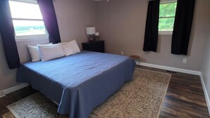 Un dormitorio con una cama, ventilador de techo, mesita de noche, ventana con cortinas y una alfombra estampada.