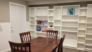 Un comedor con mesa y sillas de madera, rodeado de estanterías blancas con libros y objetos decorativos.