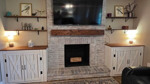 Una sala de estar con chimenea, televisor montado y estanterías decorativas.