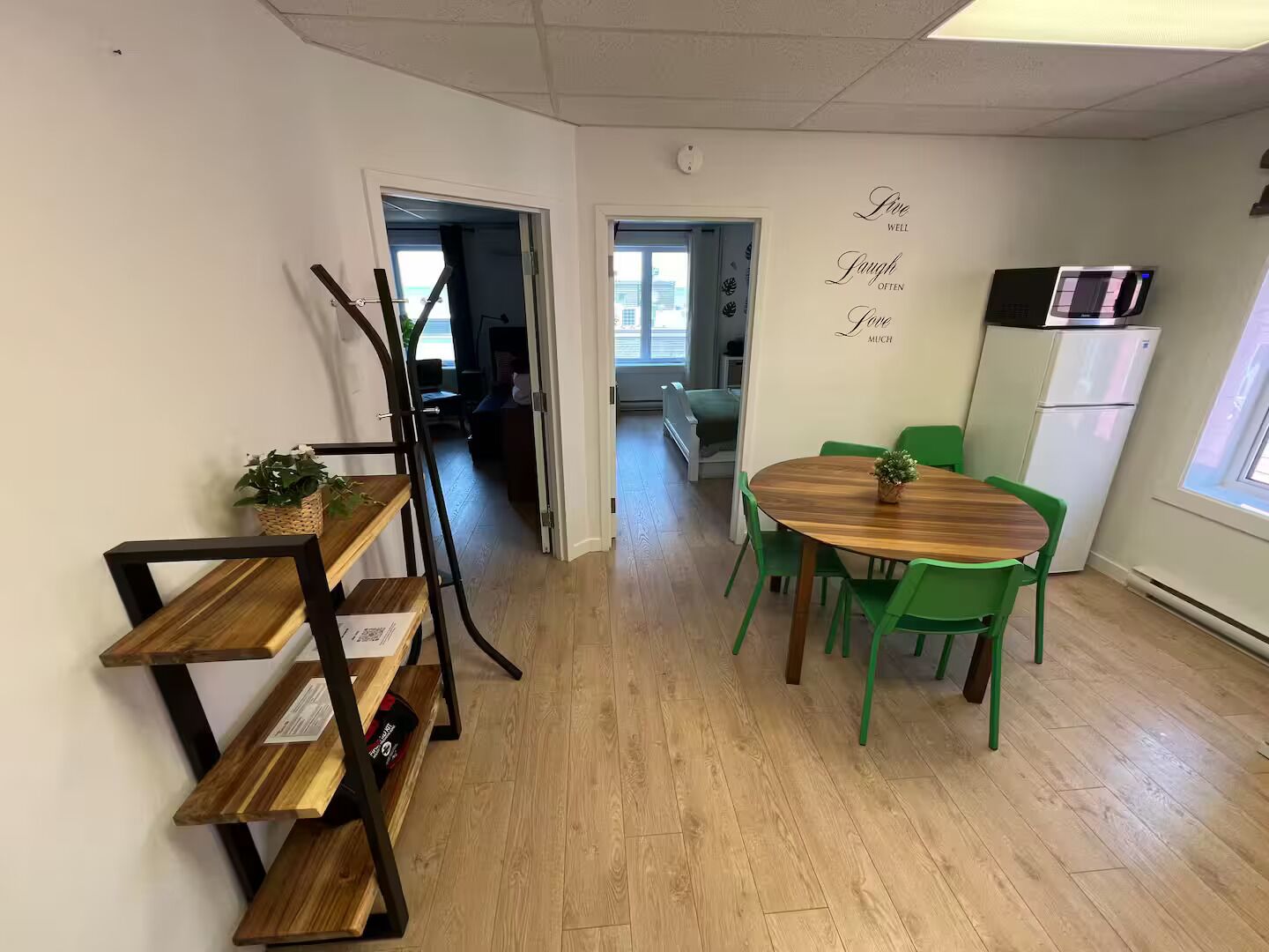 Een eetruimte met een houten tafel en groene stoelen, een keuken met een magnetron, en een wand met motiverende tekst.