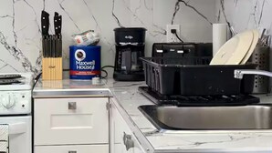 A kitchen with a white stove, a coffee maker, and a dish rack. - Apartment EST (Rimouski)