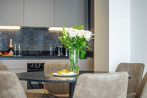 Un espace repas moderne avec une table ronde, des chaises, un vase de fleurs et une cuisine en arrière-plan.