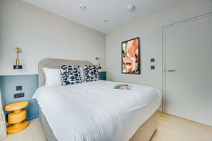 Ein ordentlich eingerichtetes Schlafzimmer mit einem großen Bett, Nachttischlampen, einem Wandbild und einer Tür.