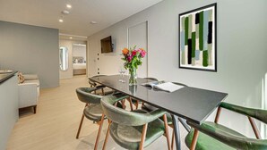 A modern dining area with a long table, green upholstered chairs, a vase with flowers, and a framed abstract painting on the wall. - Two-Bedroom Apartment at Farringdon by Dmontrio (London)
