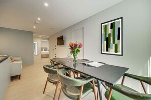 A modern dining area with a long table, green upholstered chairs, a vase with flowers, and a framed abstract painting on the wall. - Two-Bedroom Apartment at Farringdon by Dmontrio (London)