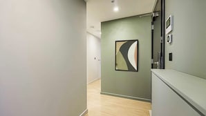 A hallway with a modern design, featuring a light-colored wall, a wooden floor, and a framed abstract artwork. - Two-Bedroom Apartment at Farringdon by Dmontrio (London)