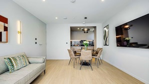 A modern living room with a sofa, dining table, and chairs, a kitchen in the background, and recessed ceiling lighting. - Two-Bedroom Apartment at Farringdon by Dmontrio (London)