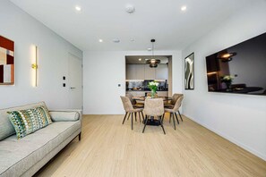 A modern living room with a sofa, dining table, and chairs, a kitchen in the background, and recessed ceiling lighting. - Two-Bedroom Apartment at Farringdon by Dmontrio (London)