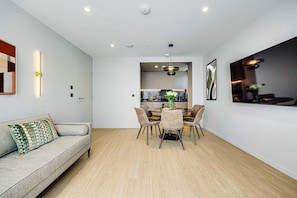 Ein modernes Wohnzimmer mit Sofa, Esstisch und Stühlen, im Hintergrund eine Küche und Deckenleuchten.